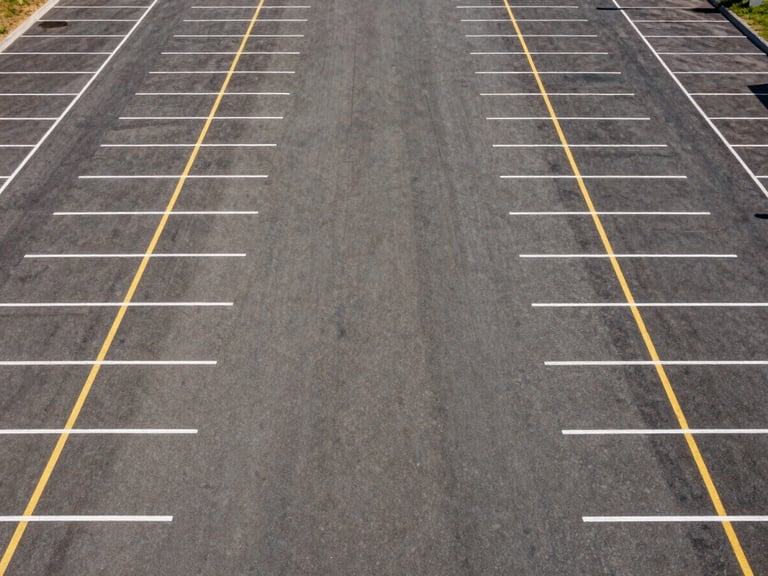 High-angle drone shot of a massive, perfectly striped empty commercial parking lot with crisp white and yellow lines, stark midday sun.