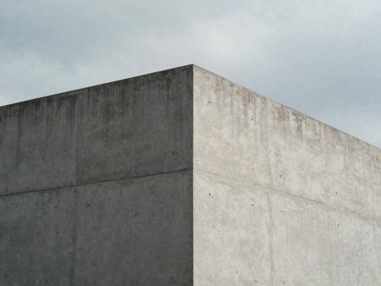 Minimalist architectural corner of a concrete building under cool overcast daylight, sharp geometric shadows, desaturated cool tones, 35mm photography.