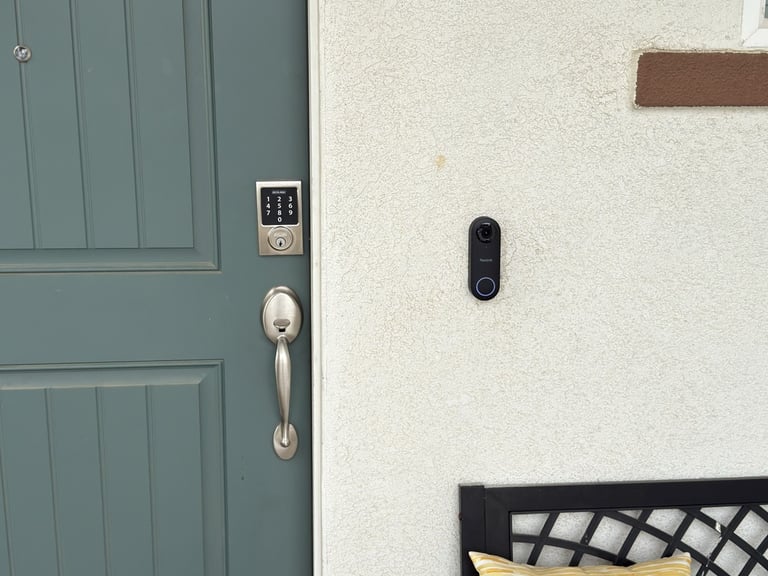 A teal front door video doorbell camera installed on the white stucco wall.