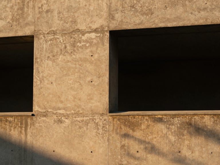 Close-up of concrete textures and dramatic shadow play on a minimalist building facade, golden hour light.