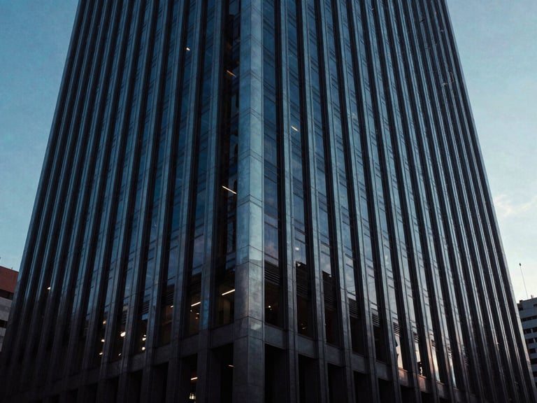 Wide panoramic shot of a modern corporate skyscraper facade in Monterrey at dusk, cool steel-blue tones, sharp architectural lines, dramatic low-key lighting.