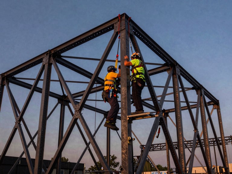 Primer plano de un técnico inspeccionando una estructura de truss de escenario robusta, con arneses de seguridad y fondo de un cielo despejado.