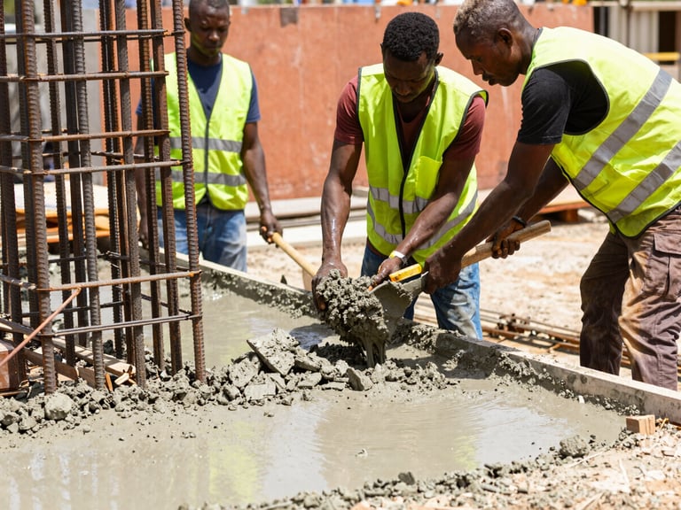 A close-up of Nigerian construction workers in high-visibility vests pouring and leveling wet concrete around thick steel rebar on a sunny Lagos site