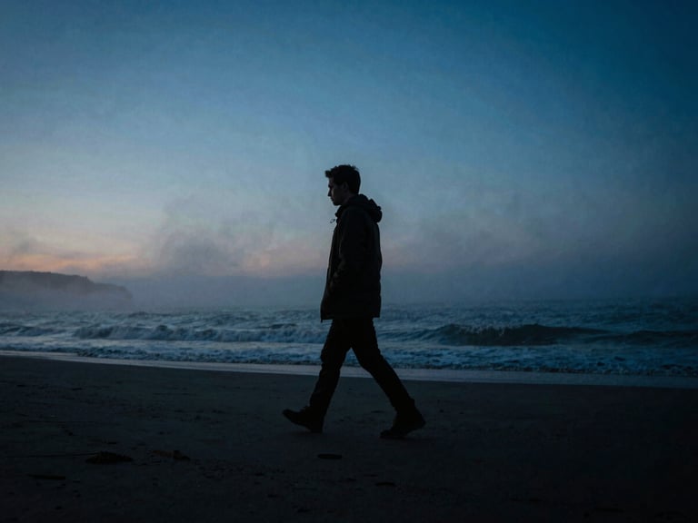 Cinematic wide shot of a solitary figure walking along a misty coast at dawn, cool blue key lights mixed with low-key dramatic lighting, high-contrast chiaroscuro.