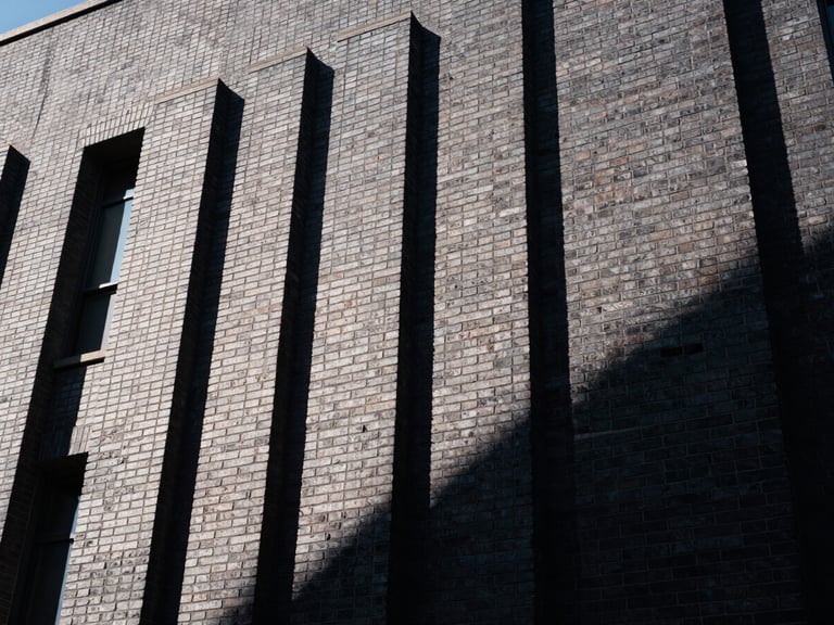 Low-angle architectural shot of a massive commercial brick facade, sharp afternoon sunlight casting crisp geometric shadows, deep charcoal masonry joints, 35mm photography.
