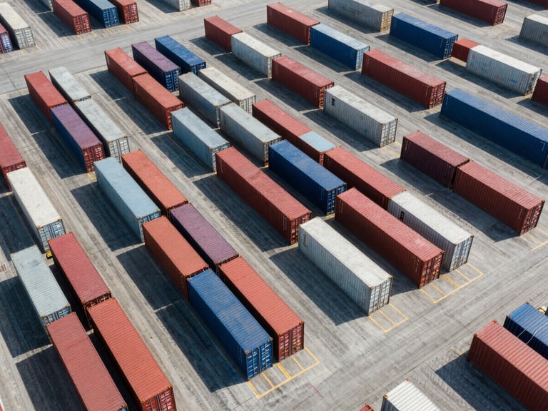 Wide-angle drone shot of an industrial logistics hub, rows of shipping containers, overhead view, crisp geometric shadows, bright daylight.