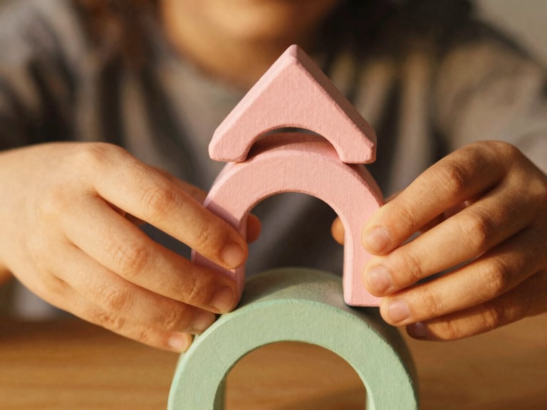 Close-up of child's hands carefully stacking beautifully painted wooden arches in dusty rose and sage green, warm soft golden light, shallow depth of field, 35mm