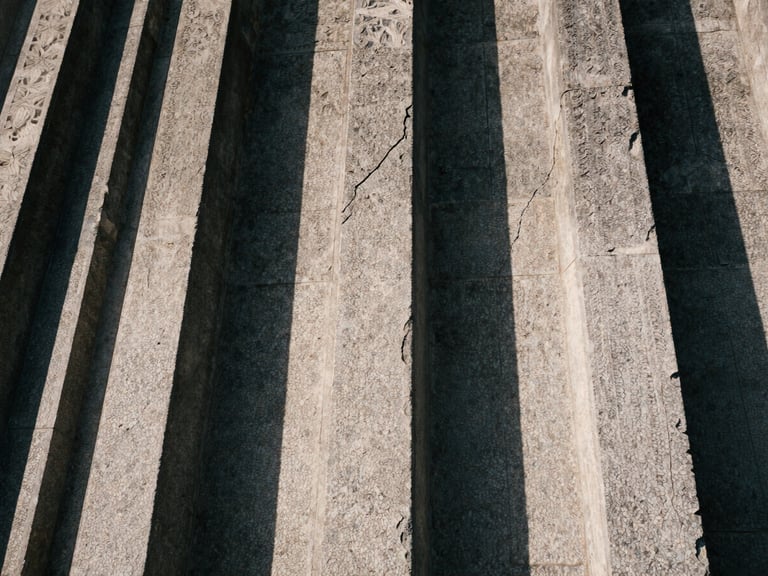 Extreme close-up of weathered stone carvings on a historic building facade, deep shadows highlighting the cracks and erosion
