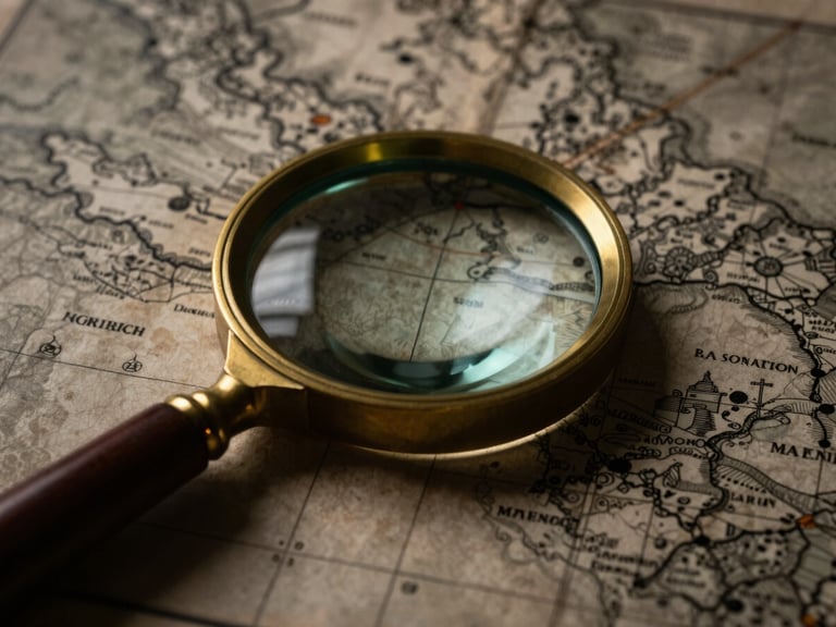 Close-up of a vintage brass magnifying glass resting on a detailed game map printed on aged parchment, dramatic low-key lighting, deep shadows, macro lens