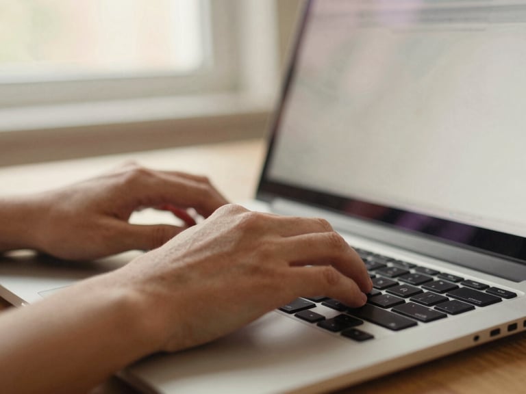 Close-up of hands typing on a laptop keyboard, screen showing a clean, modern interface, warm light from a window, shallow depth of field, 35mm.