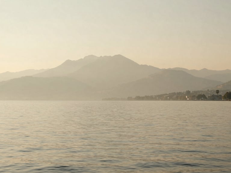A quiet afternoon on Lake Geneva, soft light reflecting on the calm water, distant mountains in a hazy warm beige mist, minimalist composition.