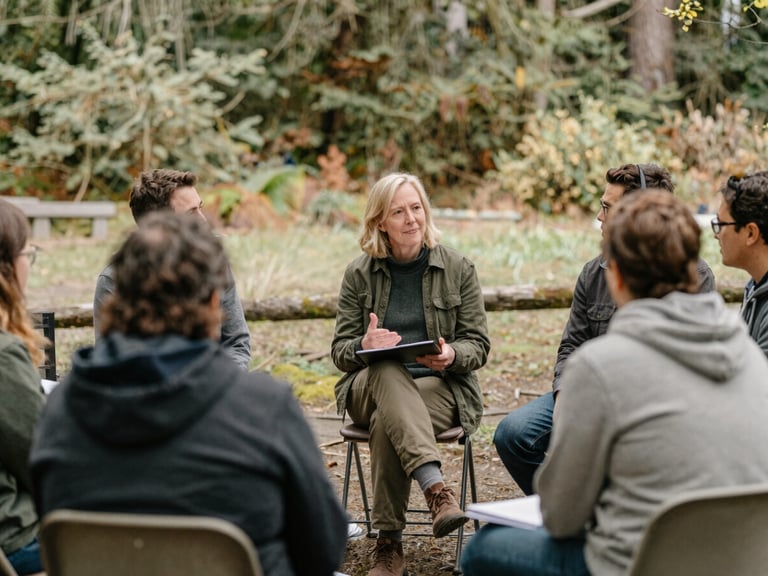 Washington community leader facilitating a small group discussion outdoors, natural Pacific Northwest daylight, soft earthy tones, candid interaction, 35mm lens.