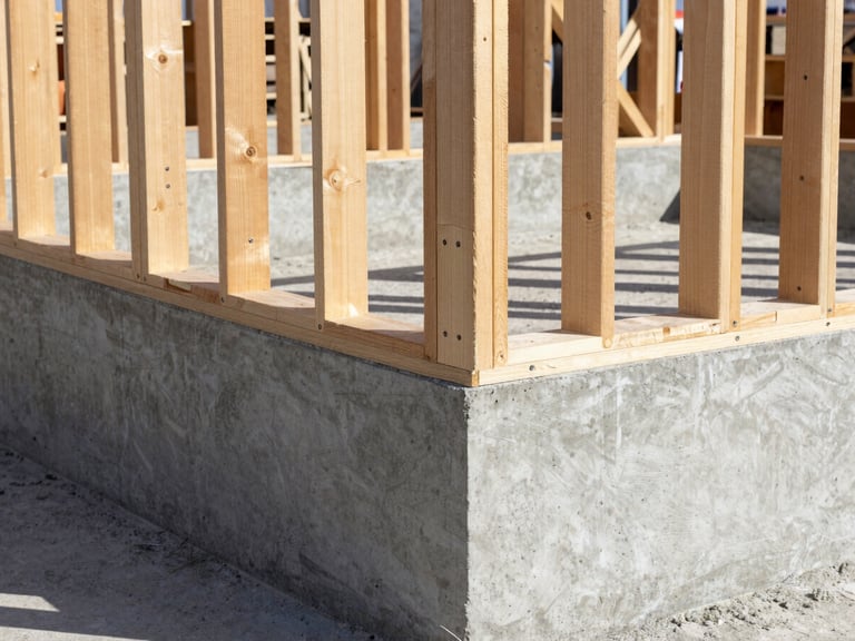 Close-up of freshly poured concrete foundation and pristine structural timber framing under bright daylight