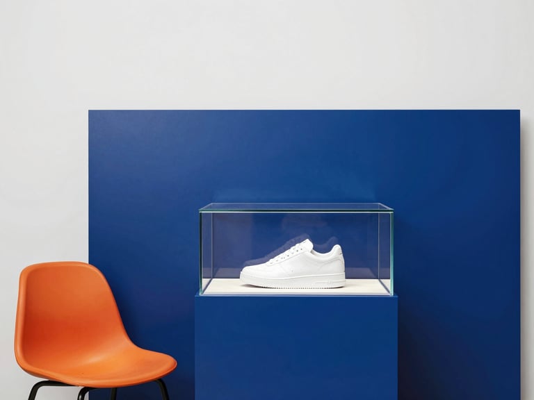 Interior shot of a private, minimalist showroom suite, deep blue accent wall, a comfortable chair, and a display case with a single, pristine rare sneaker, bright studio light, no people visible