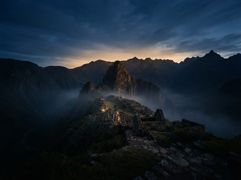 Wide panoramic shot of a subtle Andean mountain range at dawn, soft mist, ancient stone structures barely visible, warm golden light, low horizon.