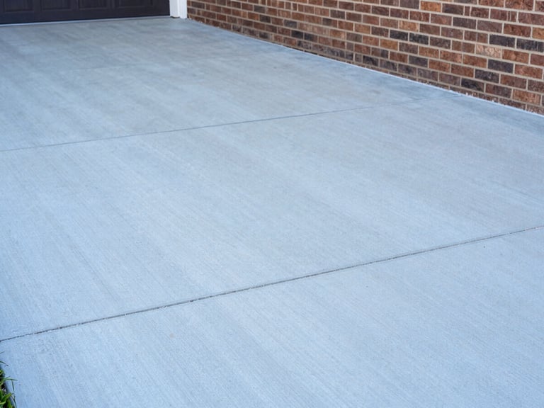 Close-up of clean concrete driveway next to brick siding, showing sharp contrast between washed and unwashed areas, bright daylight, sharp focus, 35mm