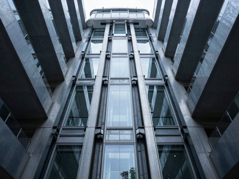 Low-angle symmetrical architectural photograph of a sleek glass elevator shaft rising through a modern steel atrium, cool daylight, high-contrast steel textures.