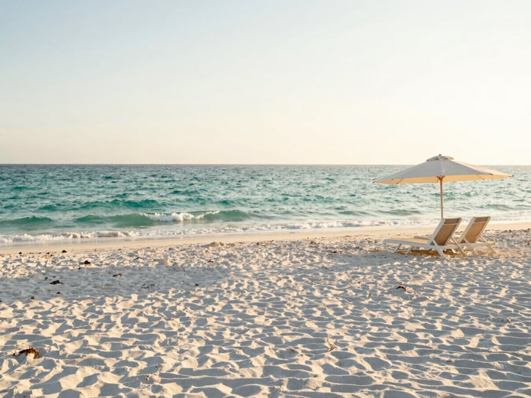 Wide panoramic view of a pristine white sand beach in Miramar Beach, gentle emerald waves, a few elegant beach chairs under an umbrella on the right, soft afternoon sun.