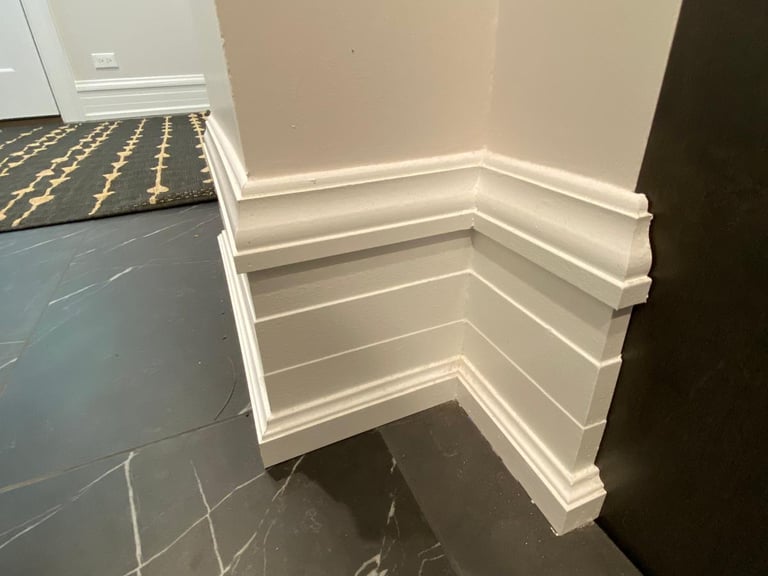 Elegant white baseboard and decorative wall trim installed above black marble floor tiles.