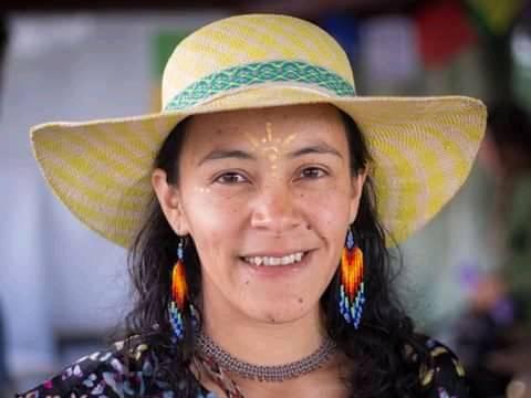 Mujer sonriente usando un sombrero tejido y vibrantes aretes indígenas de chaquiras.