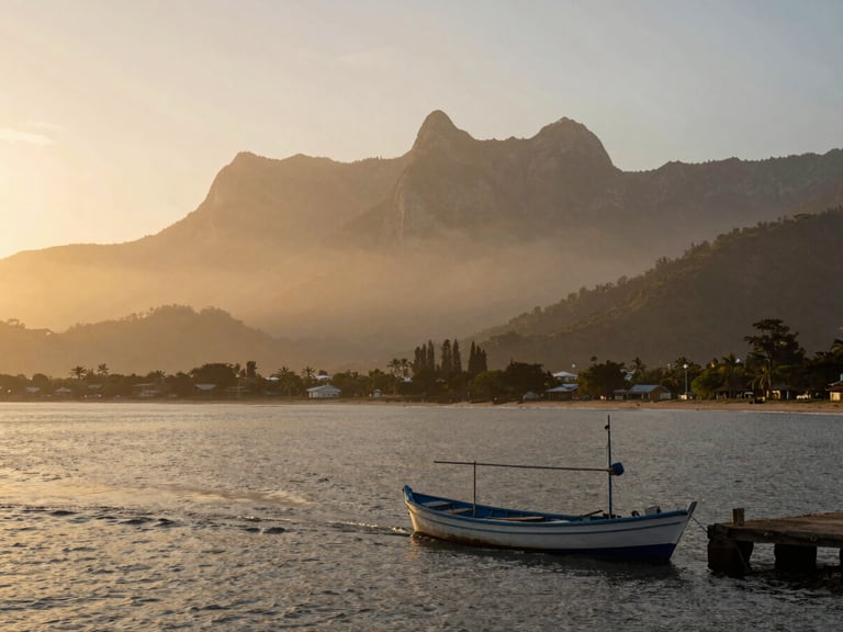 Wide environmental shot of Santa Marta bay at morning light, Sierra Nevada peaks visible in the misty background, a narrow fishing boat leaving the dock in the foreground, golden warm tones on the water surface