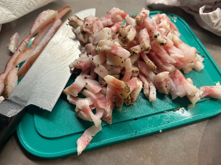 Slices of raw guanciale cured pork jowl with black pepper on a green cutting board.