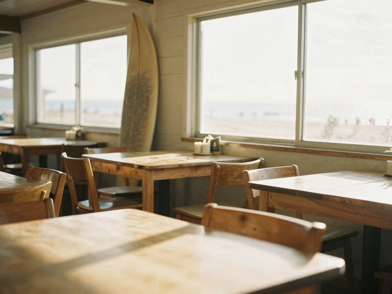Bright environmental shot of a cozy coastal cafe interior with light wood tables, vintage surfboards leaning against the wall, and warm golden-hour sunlight streaming through the windows, 35mm.