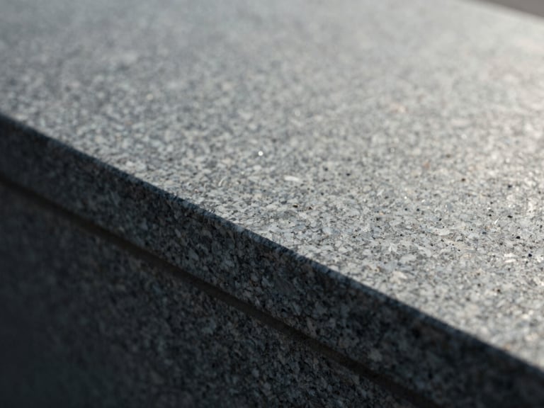 Macro detail shot of dark gray granite texture catching soft morning sun, showing deep crystalline grain, 35mm film texture