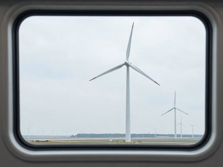 Scenic view of modern wind turbines and a distant runway framed perfectly through a clean, double-paned train window, cool overcast daylight, sharp focus.