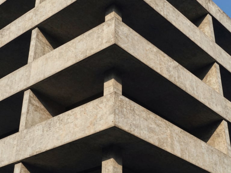 Tight abstract crop of a concrete building corner, architectural geometry, strong shadows, crisp natural daylight, deep navy and warm amber tones.