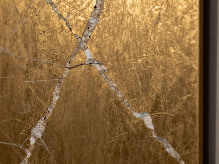 Macro detalhe de mármore italiano com veios dourados profundos justaposto a uma placa de bronze escovado, iluminação lateral dramática destacando as texturas nobres.