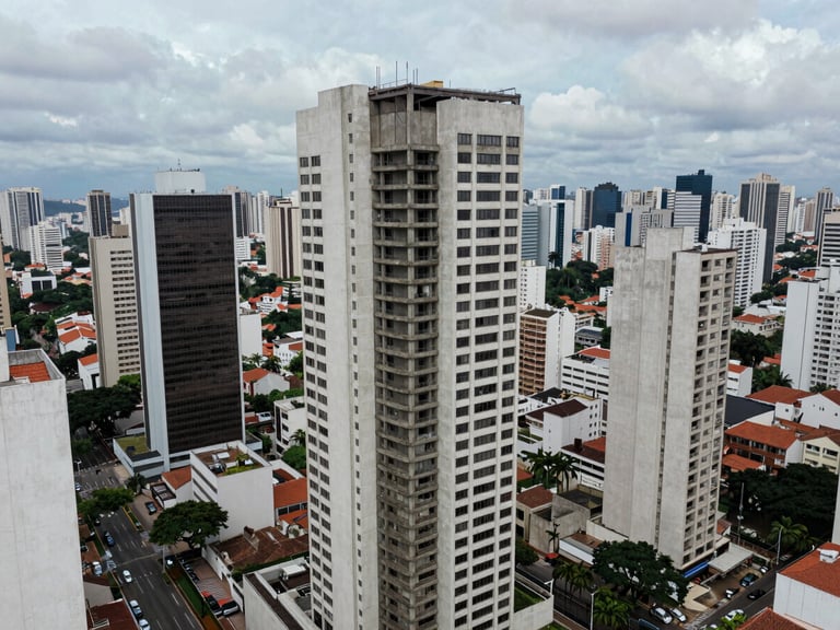 Wide aerial view of a completed commercial high-rise in the São Paulo metropolitan area, structural concrete core visible at rooftop, overcast diffuse light, surrounding urban context in frame, no people