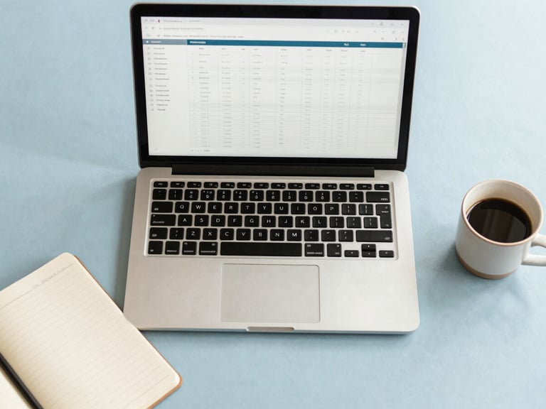 Overhead flat-lay of an organized modern desk with a sleek laptop showing clean spreadsheets, a neat notebook, and a ceramic coffee cup in soft morning light.