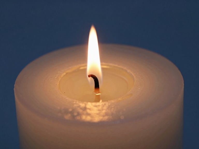 Macro shot of a burning candle wick, warm golden flame casting light on a pooling clear oil, deep blue background, shallow depth of field.