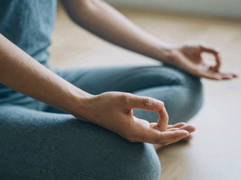 Close-up of hands in a gentle meditative mudra resting on a knee, soft diffused morning daylight, muted earthy blue tones, serene film photography.