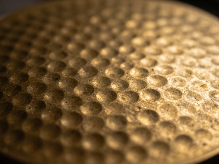 Close-up macro shot of textured hammered brass with a warm golden patina, shallow depth of field, dramatic side-lighting showing metallic ridges.