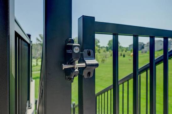 Close-up of a lockable black metal safety latch on a backyard deck gate for pool security.
