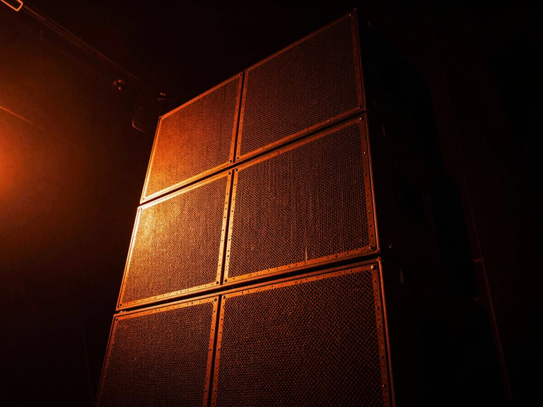 Dramatic low-key photo of a massive speaker stack on a dark stage, vibrant electric orange light leaks, gritty texture, wide angle.