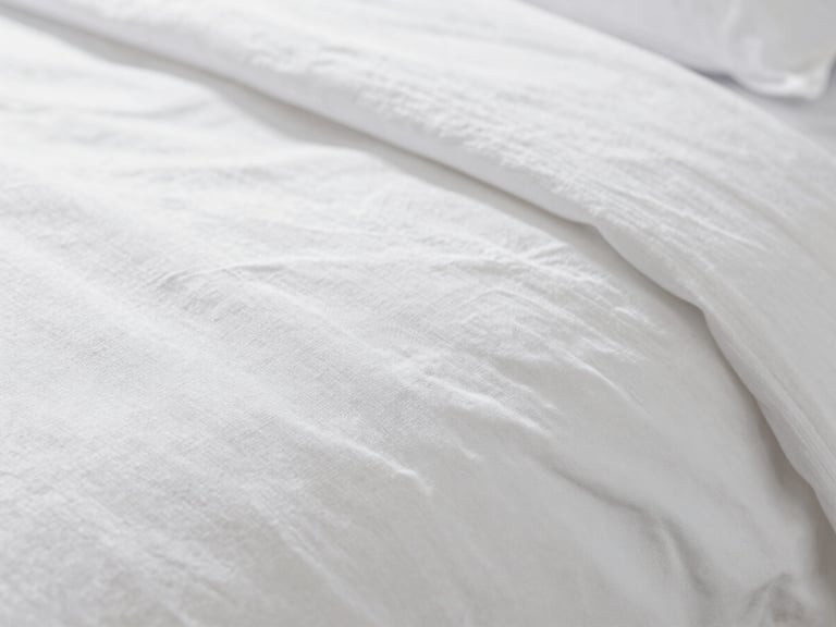 Macro close-up of crisp white long-staple combed cotton bed sheet texture, showing fine weave and subtle sheen, soft natural window light, crisp whites and deep navy tones, shallow depth of field, 35mm