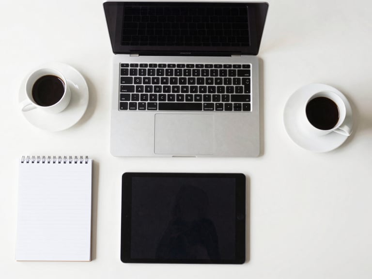 Structured overhead desk shot with modern tech tools (laptop, tablet, notepad) and a coffee, clean minimalist background, natural daylight