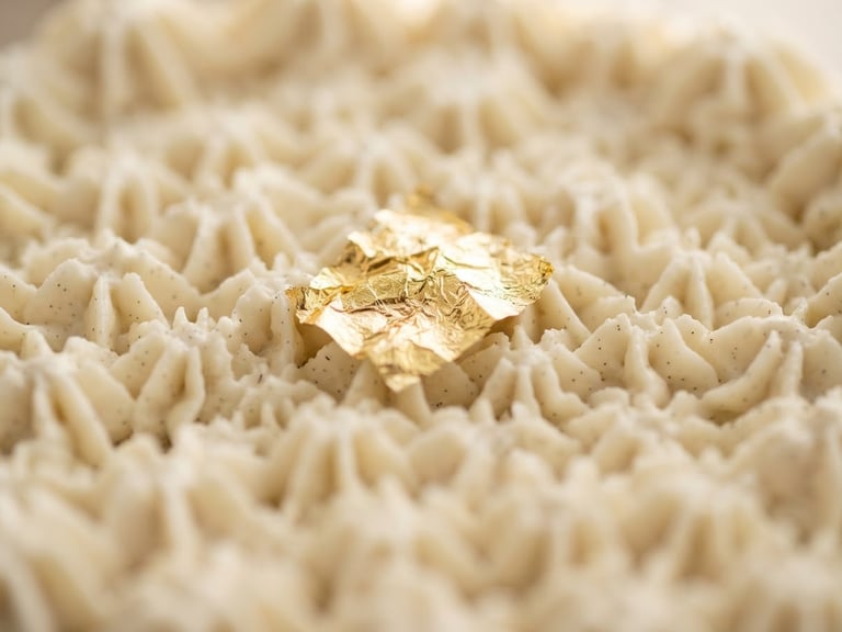 Macro shot of a pristine, hand-piped vanilla bean cake texture with a single edible gold leaf, soft morning light, shallow depth of field