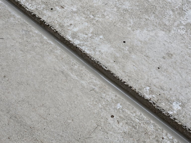 Tight close-up overhead shot of raw concrete substrate surface beside a freshly applied epoxy coating edge, showing the material transition zone, existing warehouse ambient light, no people, surface grain and pore detail clearly visible