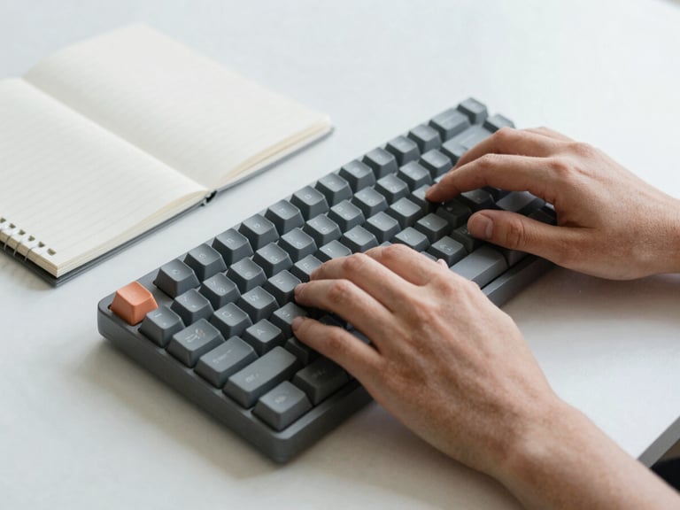Close-up of hands typing on a mechanical keyboard next to a clean notebook, neutral daylight, cool gray and slate tones, 35mm