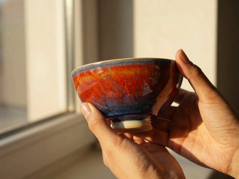A pair of hands gently holding a vibrant ceramic bowl, inspecting its glaze and form, warm golden-hour light, tactile textures.