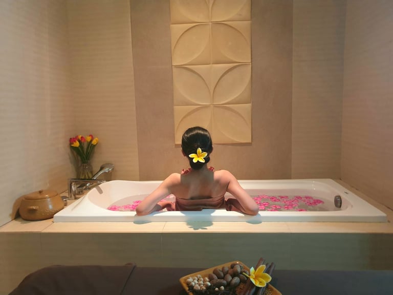 A woman relaxes in a luxury spa bathtub filled with pink flower petals for a wellness treatment.