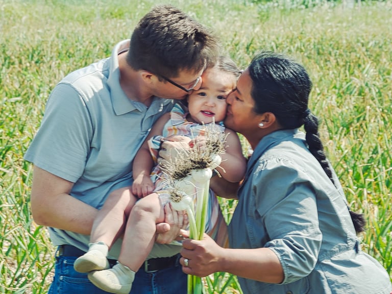 a man and woman holding a baby in a garlic field
