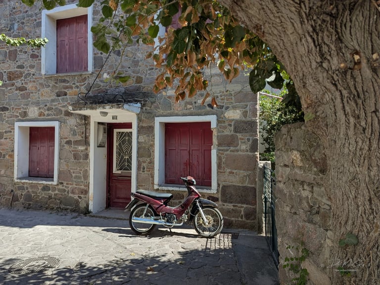 old burgundy moped in front of a stone house with burgundy shutters in Petra, Greece