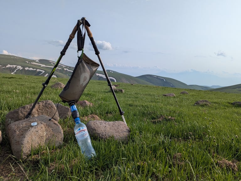 A water bladder is suspended between two trekking poles filtering water through a sawyer squeeze.