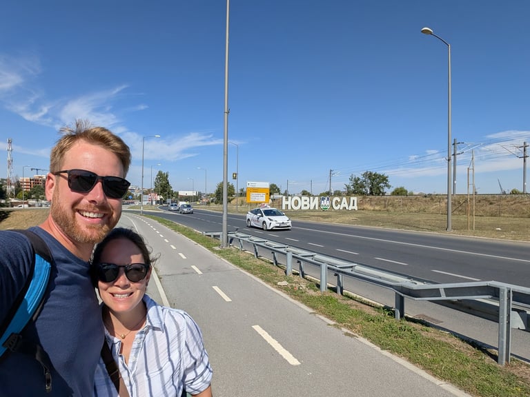 Don and samantha next to a highway road sign that sayd Novi Sad in Cyrillic 
