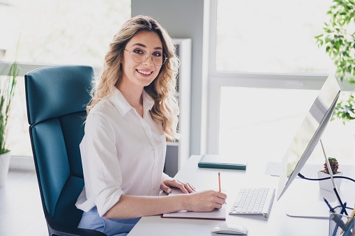 Une femme, secrétaire, assistante administrative, assise à son bureau devant un ordinateur